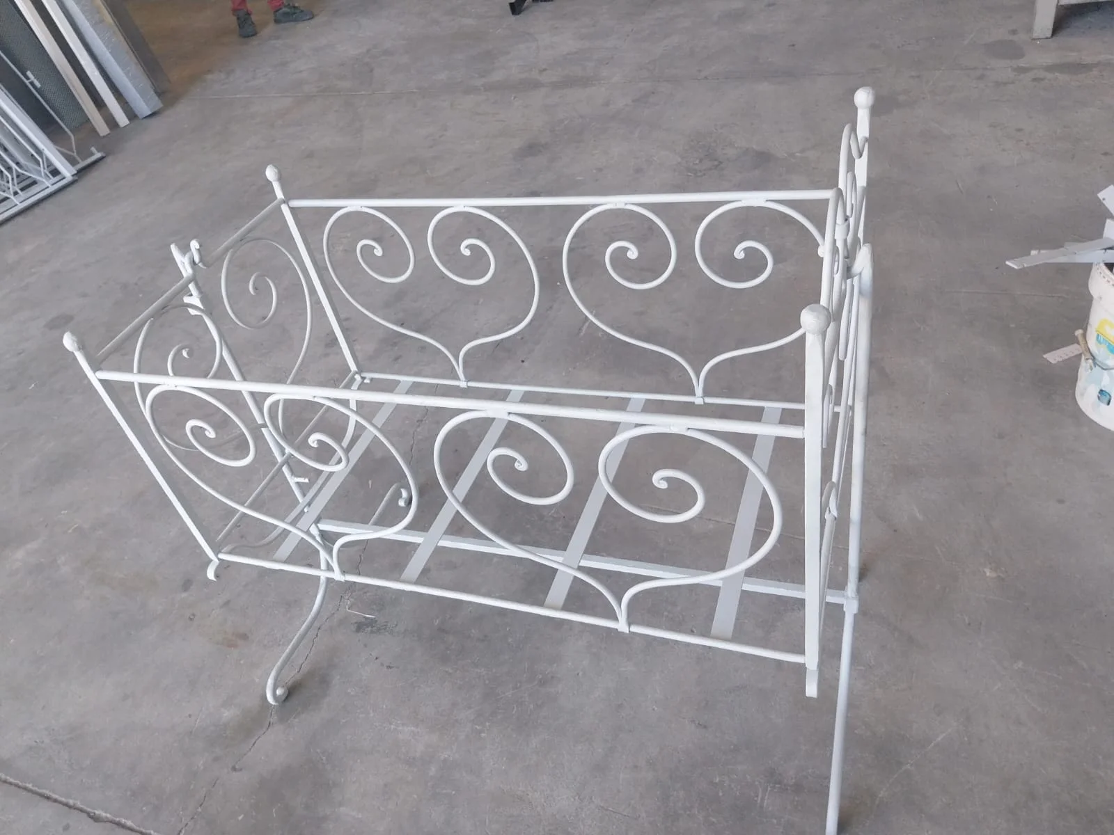 Estrutura de cama metálica clara, com volutas.